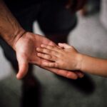 Bir çocuğun elinin bir yetişkinin elinin üzerinde durduğu babalık ve soybağı temalı görsel